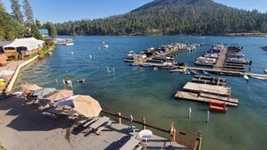 A marina with boats docked, a dock with sun loungers, and a forested hill in the background. - Bass Lake | Group Lake Getaway | Pool + Lake | 2BR (Bass Lake)