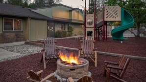 A fire pit with chairs around it, a playground, and a building in the background. - Bass Lake | Group Lake Getaway | Pool + Lake | 2BR (Bass Lake)