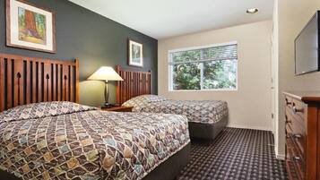 Une chambre d’hôtel avec deux lits, une fenêtre avec des stores, une lampe et un téléviseur fixé au mur.