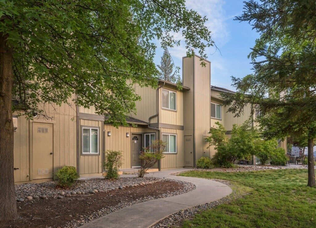 A two-story residential building with a beige exterior, a chimney, and a small front yard with a pathway.