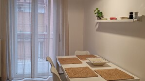 Et spiseområde med et hvidt bord, fire stole, vævede underlag, en hængende lampe og et vindue med lette gardiner.