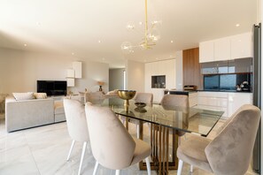A modern kitchen with a glass dining table, white cabinets, and a built-in oven. - El Dourado House | Ocean View (Caniço)