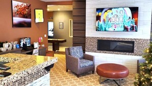 Eine Lobby mit einer Rezeption, einer gemütlichen Sitzecke mit Sofa und Hocker, einem an einer gefliesten Wand befestigten Fernseher und einem Weihnachtsbaum.