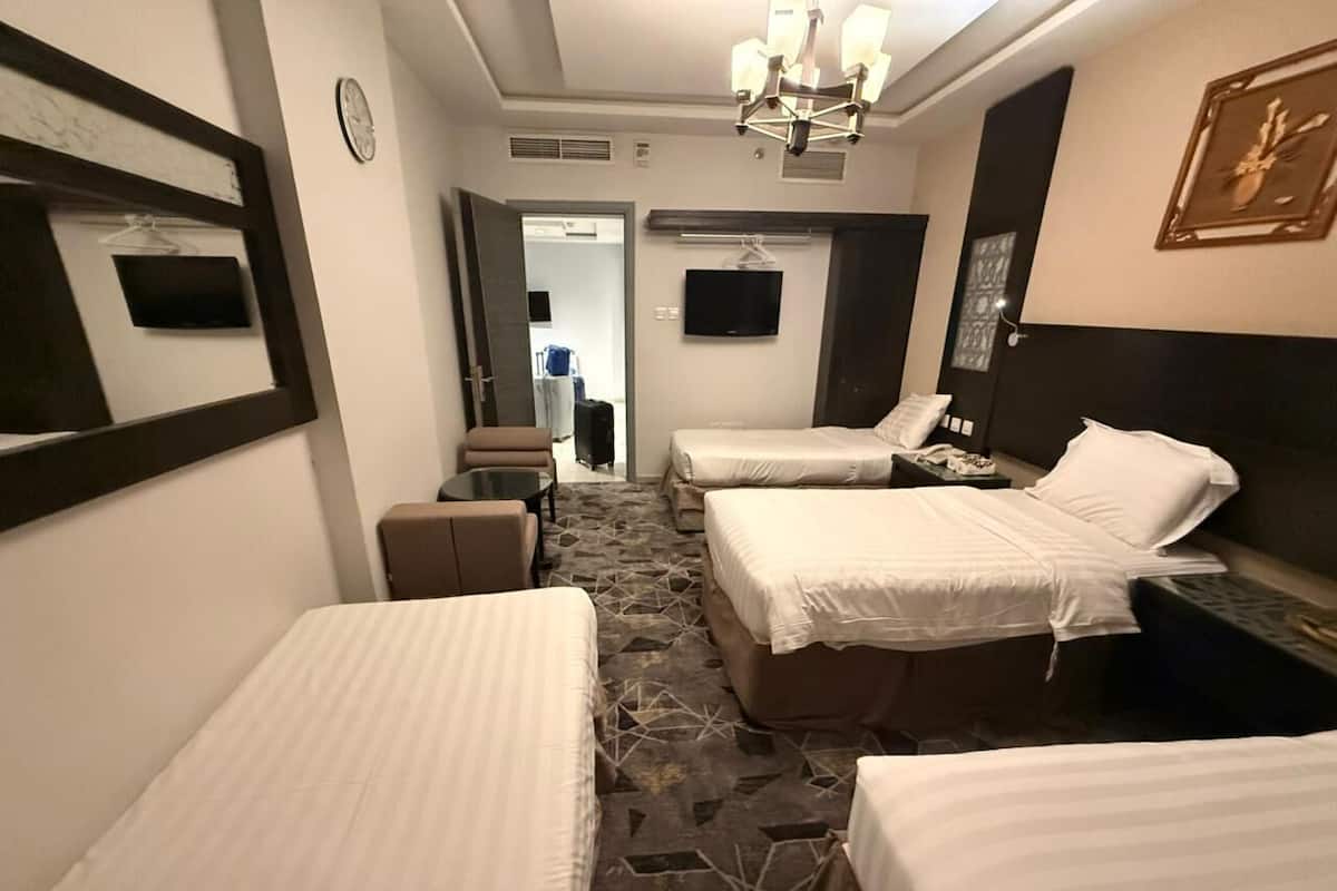 A hotel room with two single beds, a small table, a chair, a TV, and a mirror.