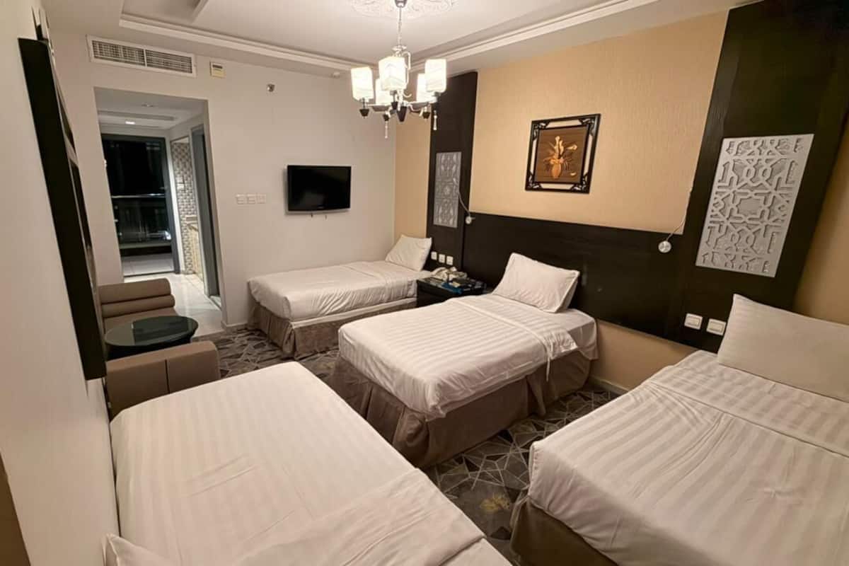 A hotel room with three beds, a TV, a chandelier, and artwork on the walls.