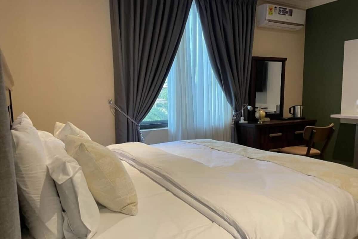 Una habitación de hotel con cama, escritorio, silla, espejo y ventana con cortinas.
