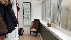 Un estrecho pasillo con suelo de madera en espiga, una silla de mimbre y un florero de vidrio con velas en el alféizar de una ventana.