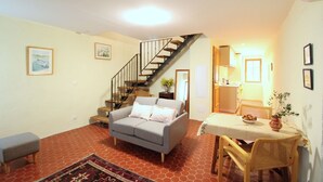 Ein Wohnzimmer mit grauem Sofa, einem kleinen Tisch mit einer Vase, einer Treppe und einem durchgehenden offenen Durchgang zur Küche.