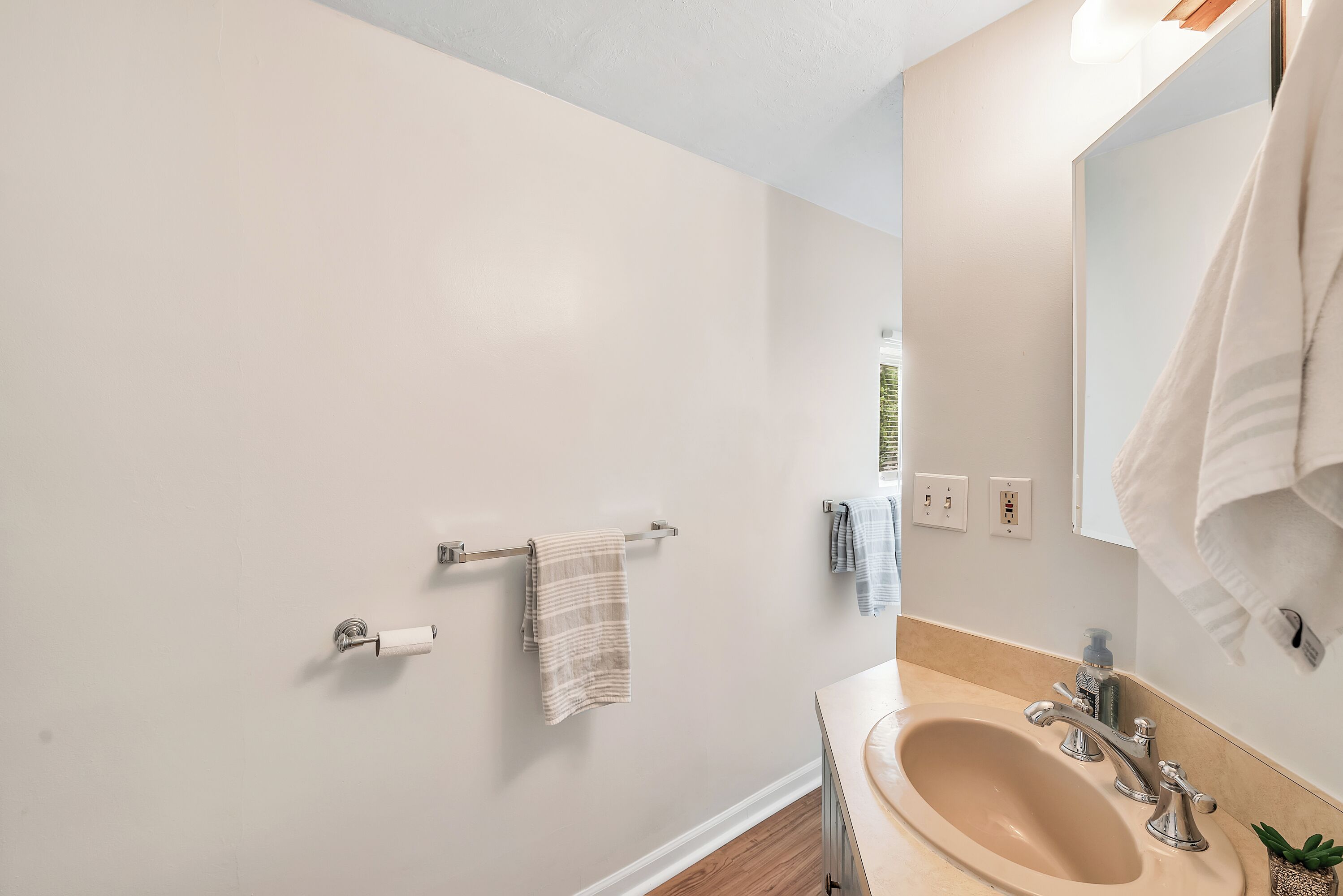 Un baño con un lavabo color beige, un espejo y un perchero con una toalla a rayas.