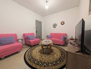 Un salon avec deux canapés roses, une table basse ronde, un tapis à motifs, un téléviseur et une porte.