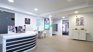 A modern reception area with a curved reception desk, a seating area with chairs, a treadmill, and a cabinet with decorative items. - Student Only Gateway Apartments (Edinburgh)