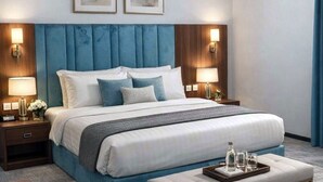 Una habitación de hotel moderna con una cama grande, dos mesitas de noche con lámparas, un cabecero y dos obras de arte enmarcadas en la pared.