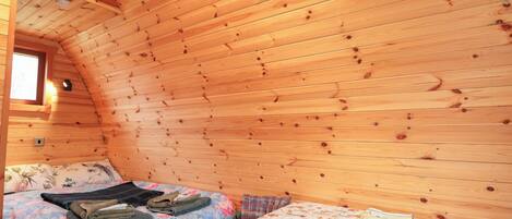 A cozy cabin room with two beds, wooden walls, a small window, and a table with a floral tablecloth.