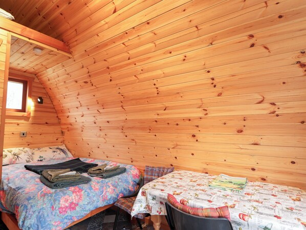 Une chambre confortable dans un chalet, avec deux lits, des murs en bois, une petite fenêtre et une table recouverte d’une nappe à motifs floraux.