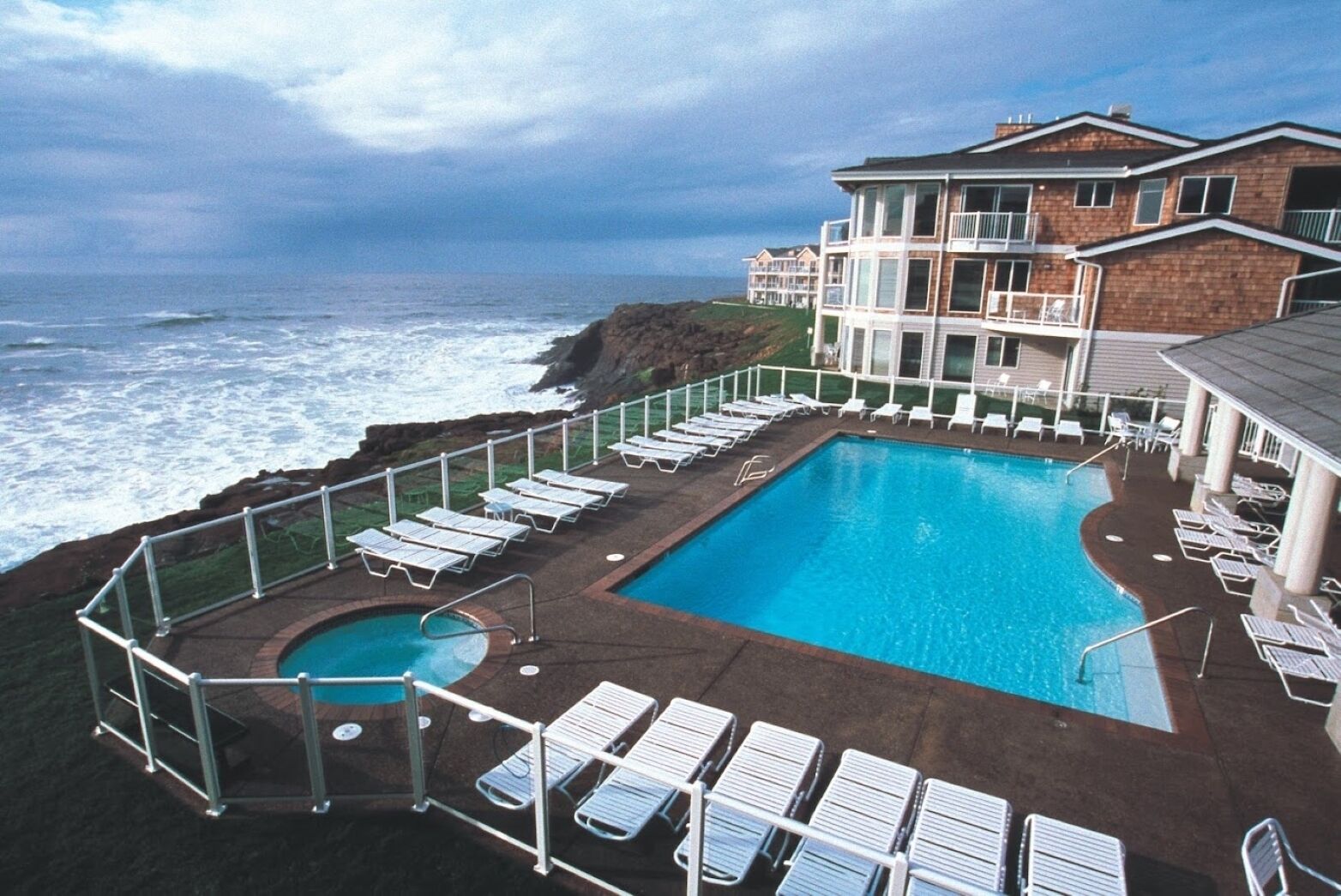 A pool area with lounge chairs and a view of the ocean.