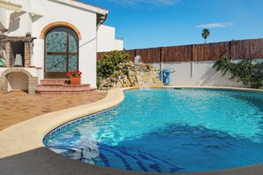 A swimming pool with a stone waterfall feature, a brick patio, and a white building with a large arched window. - Villa with its own pool, large area and beach bar 100 m from the beach (Denia)