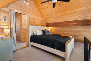 Un dormitorio tipo cabaña de madera con una cama, lámparas de noche y un ventilador de techo.