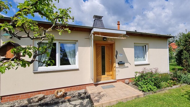 A two-story house with a wooden door, a small porch, and a garden in front. - Comfortably furnished vacation home with fireplace (Ilsenburg (Harz))