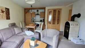 A living room with a sofa, armchairs, a coffee table, and a fireplace. There is a kitchen in the background with cabinets and a microwave. - Comfortably furnished vacation home with fireplace (Ilsenburg (Harz))
