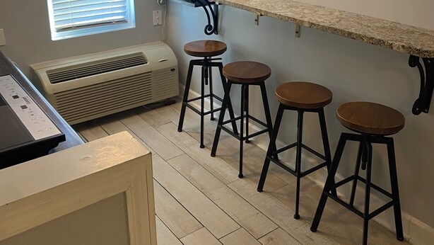 A kitchen with a countertop, four stools, a window with blinds, an air conditioner, and a ceiling light. - Condo in Gulf Shores with great location. Walk everywhere, 3mins from the beach. (Gulf Shores)