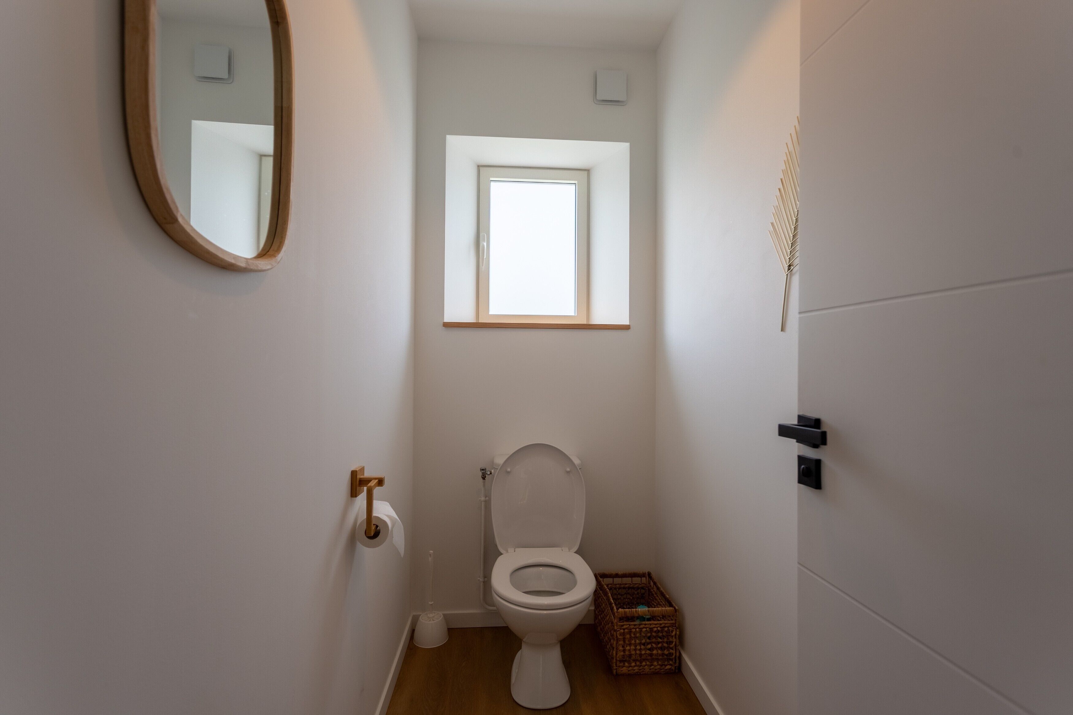 Un baño pequeño y limpio con inodoro, ventana, espejo y una cesta.