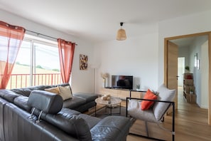 Un salon moderne avec un canapé en cuir, une table basse, un téléviseur et un coin repas comprenant une chaise.