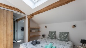 A bedroom with a skylight, wooden beams, a bed with patterned bedding, a bedside table with a lamp, and a closet with a sliding door. - Cottage in the Basque Mountains with View, Wi-Fi and Air Conditioning (Ossès)