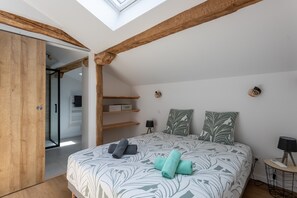 A bedroom with a skylight, wooden beams, a bed with patterned bedding, a bedside table with a lamp, and a closet with a sliding door. - Cottage in the Basque Mountains with View, Wi-Fi and Air Conditioning (Ossès)