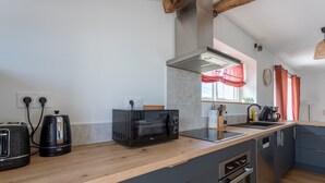 A modern kitchen with a toaster, kettle, and microwave on the counter, a built-in oven, and a window with red curtains. - Cottage in the Basque Mountains with View, Wi-Fi and Air Conditioning (Ossès)