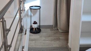 A modern, well-lit room with a wooden floor, a small round table with a plant, a metal railing, and a large window with curtains. - At sandra&fred your vacation in the dream of our cokon (Calvi)