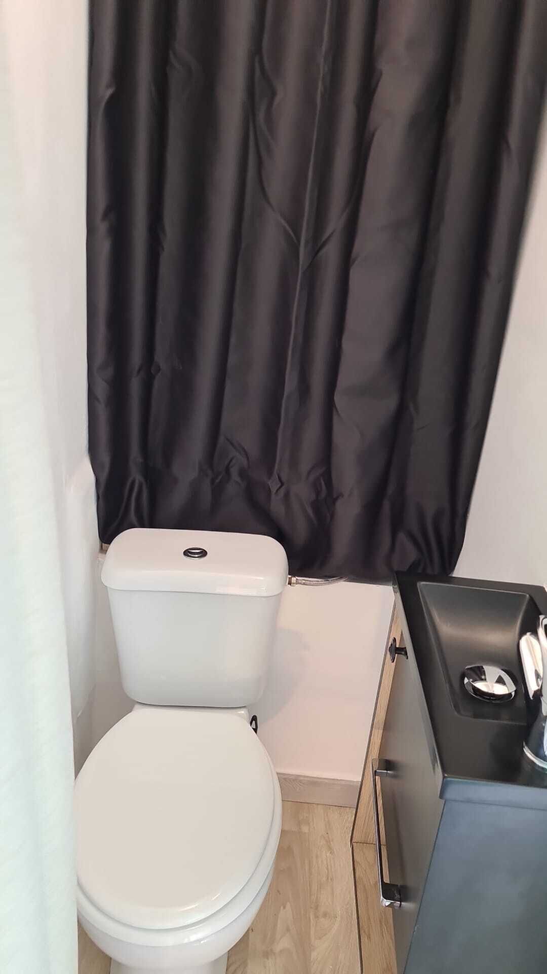 A small bathroom with a white toilet, a black curtain, and a small cabinet with a mirror.
