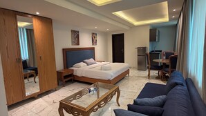 A modern hotel room with a large bed, a sofa, a coffee table, a wardrobe, and a kitchen area. - Sama Al Hamra Furnished Apartments (Beirut)