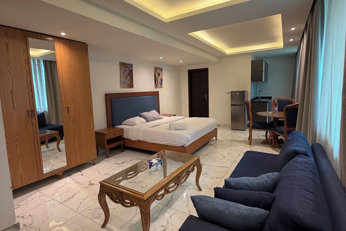 Una camera d'albergo moderna con un letto grande, un divano, un tavolino, un armadio e un angolo cottura.
