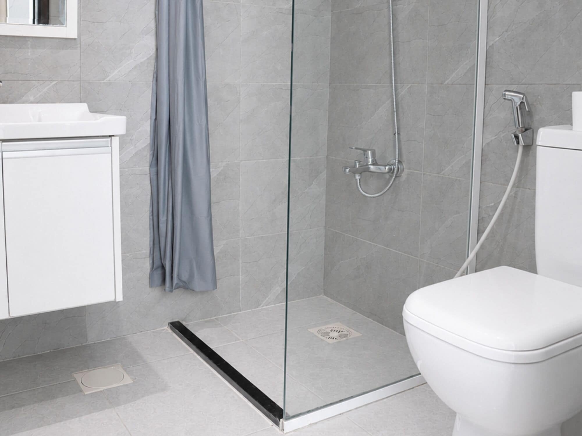 Ein modernes Badezimmer mit einer gläsernen Duschkabine, einer weißen Toilette und einem Waschbecken mit Spiegel darüber.