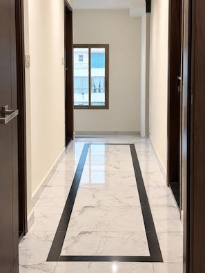 A hallway with a marble floor, a window with a view of buildings, and wooden doors. - Sama Al Hamra Furnished Apartments (Beirut)