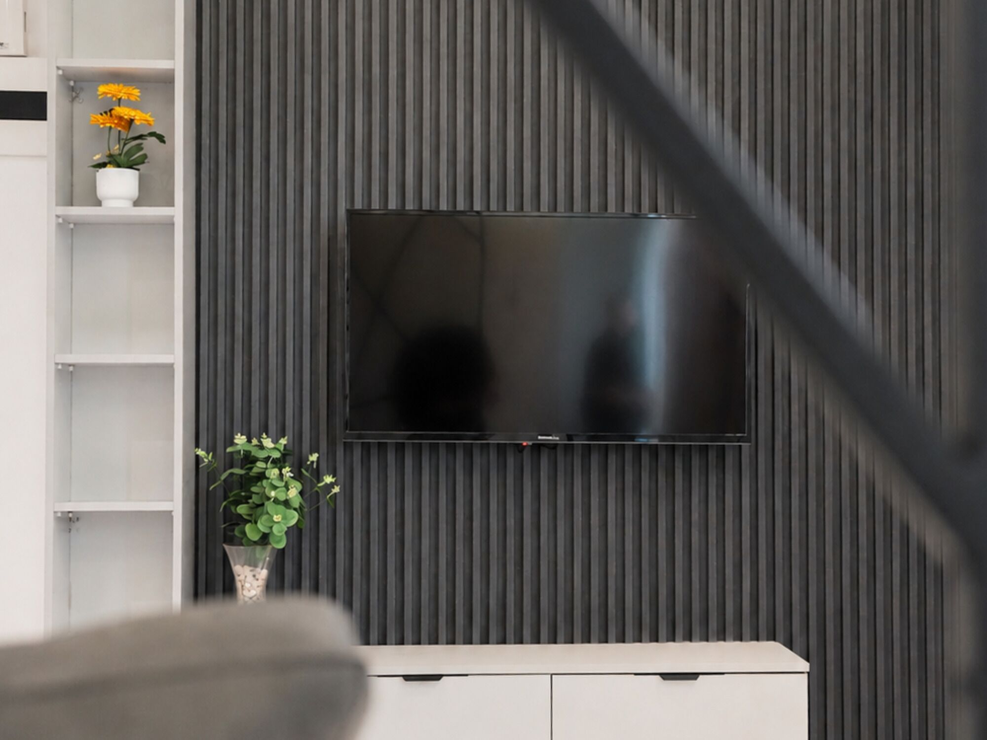 En moderne stue med et fladskærms-TV monteret på en mørk væg, et hvidt konsolbord og en hylde med en potteplante.