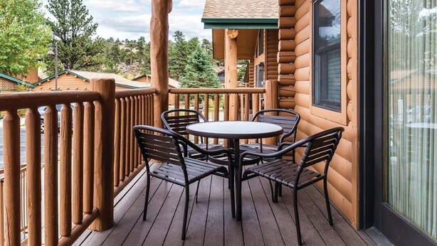 Una terraza de madera con una mesa redonda y sillas, un ventanal de vidrio y vistas del paisaje circundante.