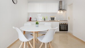 A modern kitchen with white cabinets, a round dining table with four chairs, a clock on the wall, and a microwave. - Vacation Apartment 'Nature and Calm Escape' with Mountain View and Wi-Fi (Los Silos)