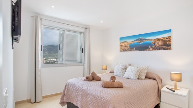 A bedroom with a bed, two bedside lamps, a painting, and a window with curtains. - Vacation Apartment 'Nature and Calm Escape' with Mountain View and Wi-Fi (Los Silos)