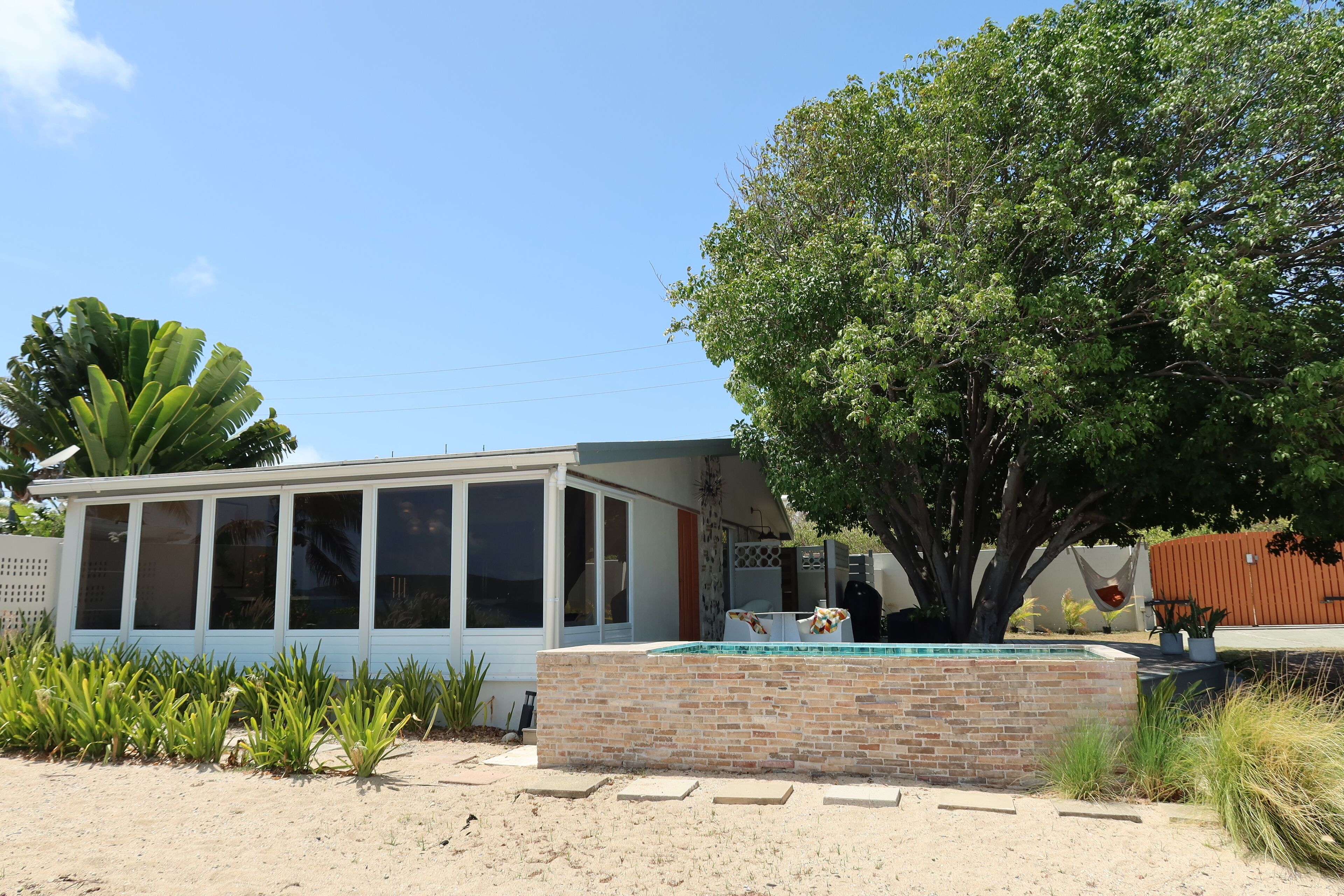 Une maison avec une piscine, un grand arbre et un espace barbecue.