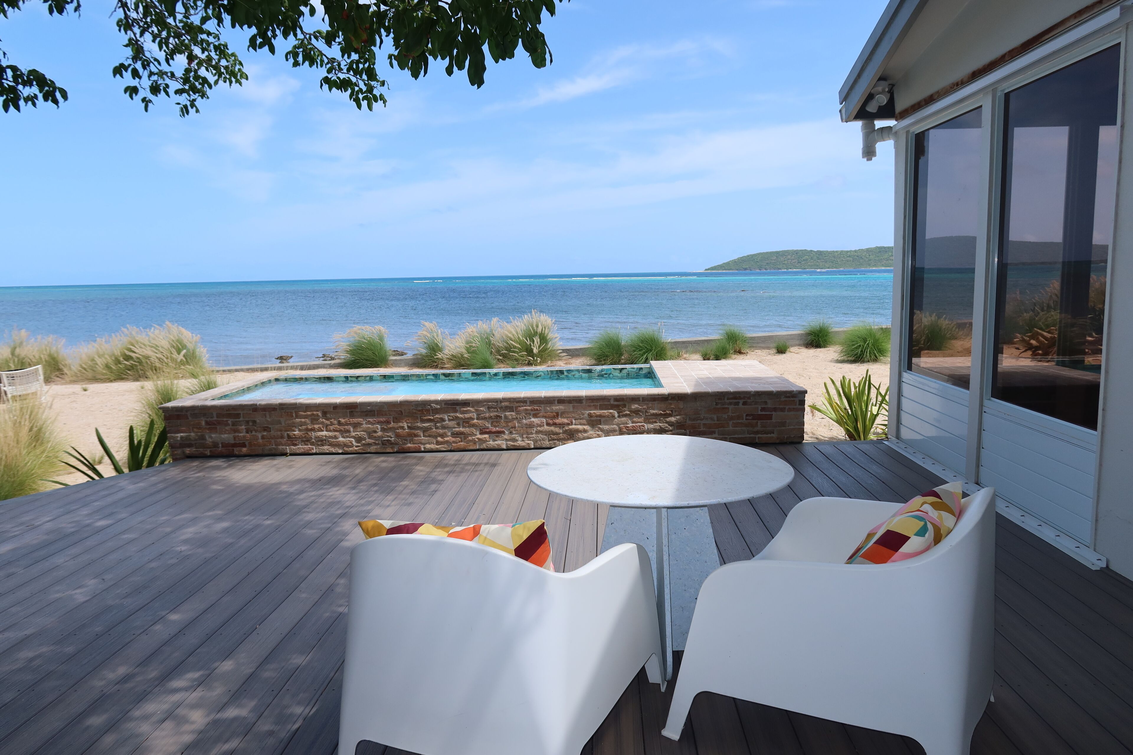 A deck with a pool, white chairs, and a view of the ocean.