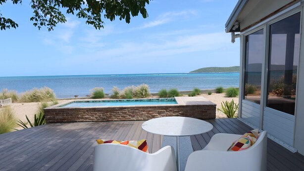 A deck with a pool, white chairs, and a view of the ocean. - Blu-Entire waterfront house (Christiansted)