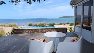 A deck with a pool, white chairs, and a view of the ocean.