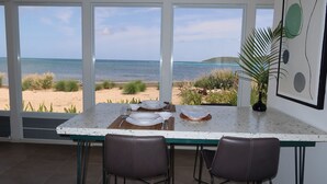 A dining area with a view of the beach and ocean, featuring a table set for two, two chairs, and a decorative plant. - Blu-Entire waterfront house (Christiansted)