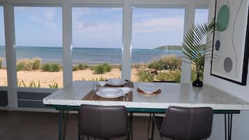A dining area with a view of the beach and ocean, featuring a table set for two, two chairs, and a decorative plant.