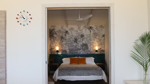 A bedroom with a bed, a ceiling fan, a wall clock, and a tropical wallpaper. - Blu-Entire waterfront house (Christiansted)