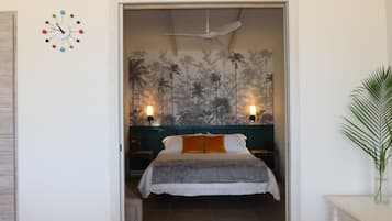 A bedroom with a bed, a ceiling fan, a wall clock, and a tropical wallpaper.