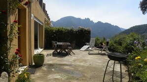 Une terrasse extérieure avec une table et des chaises, un barbecue et une vue sur les montagnes.
