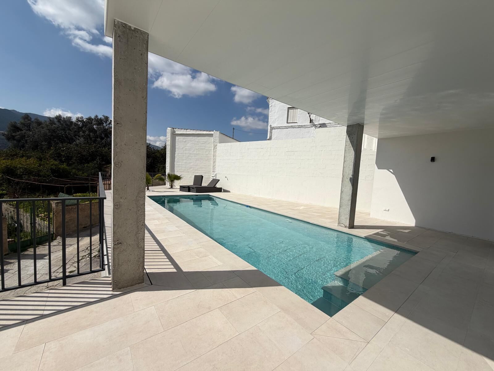 A swimming pool with a view of mountains, a white wall, and a concrete pillar.