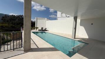 A swimming pool with a view of mountains, a white wall, and a concrete pillar.